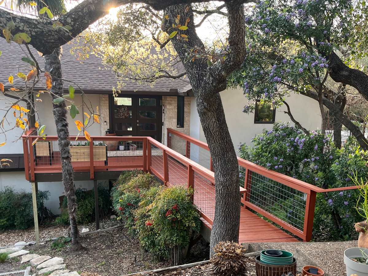 DeckRefinishing_AustinTX_1 a charming outdoor scene featuring a rustic home with a raised wooden deck and a connecting walkway.
